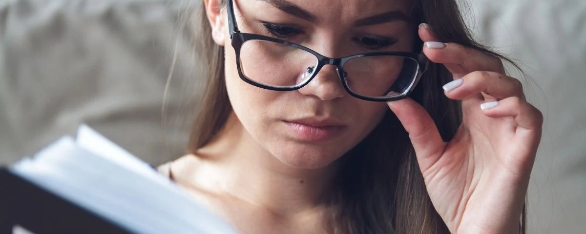 Kobieta czytająca książkę, unosząca okulary i mrużąca oczy — typowy obraz wczesnej prezbiopii